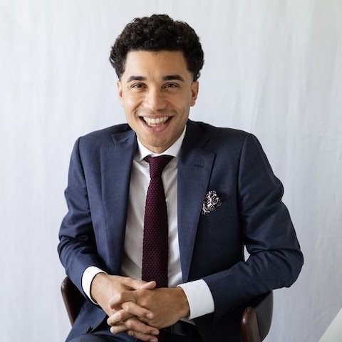 Edmar Colon smiling at the camera in a navy blue suit, white collared shirt and red tie