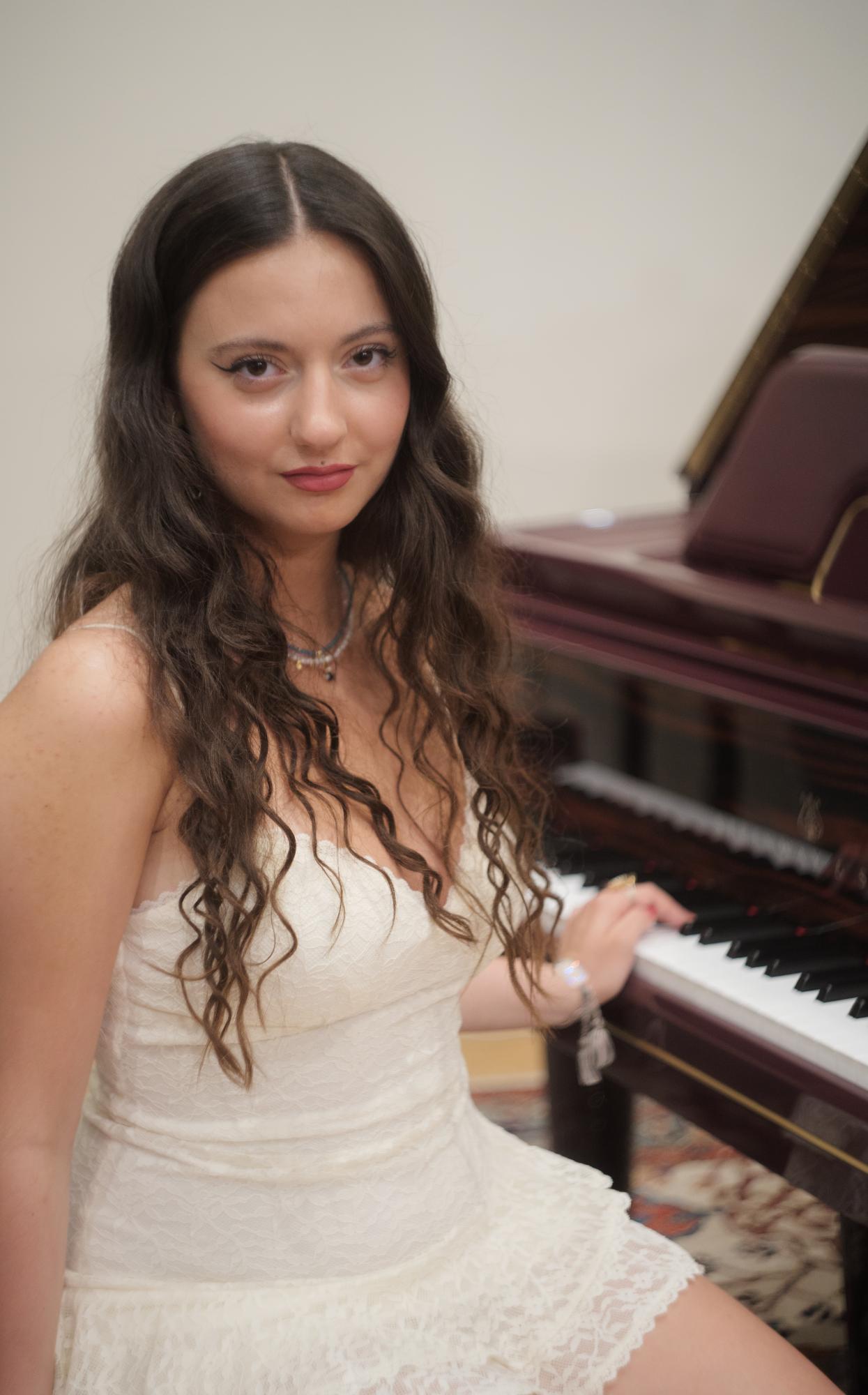 Young female pianist sits in front of a piano a smiles.