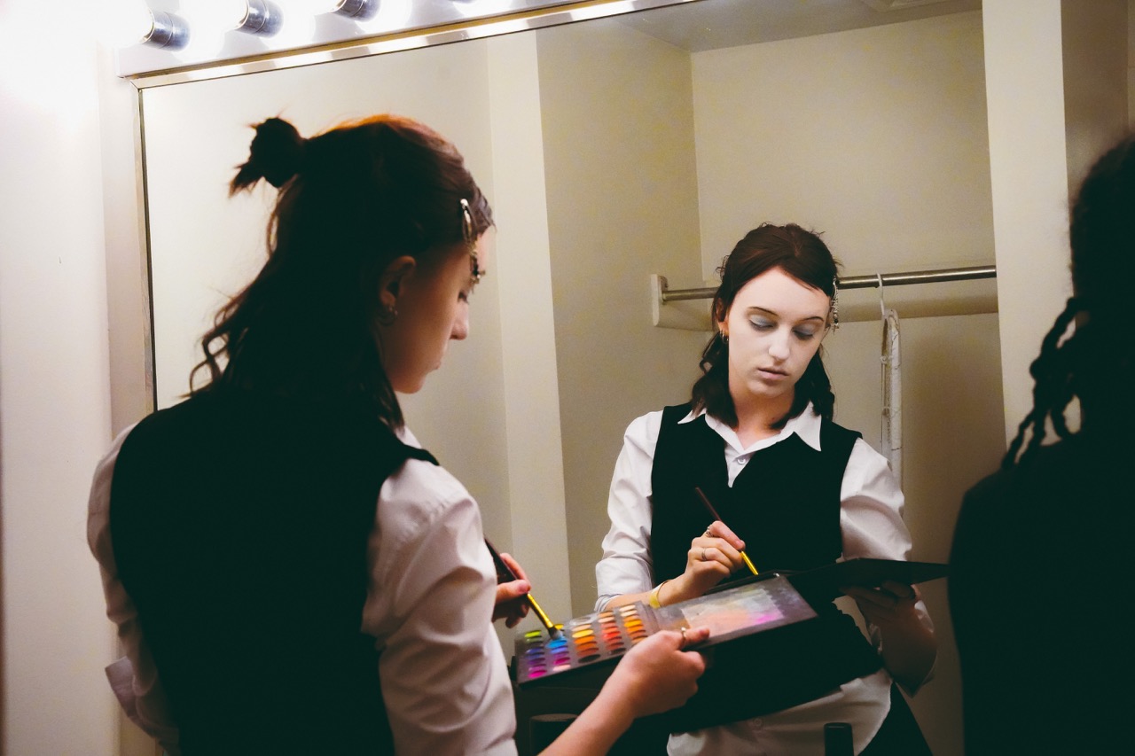 student performer getting ready in a mirror with eyeshadow palette