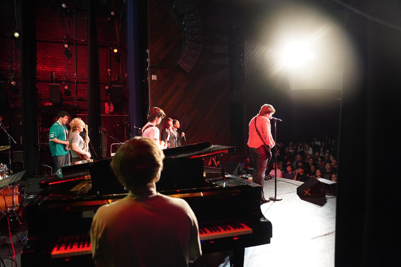 photo of a piano and a singer in the background from the back of the stage