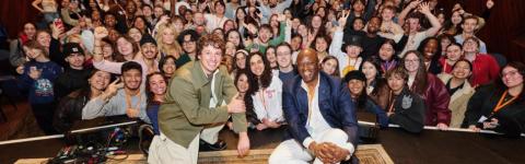 Charlie Puth and Prince Charles Alexander crouch on stage for a photo with a packed auditorium in the background