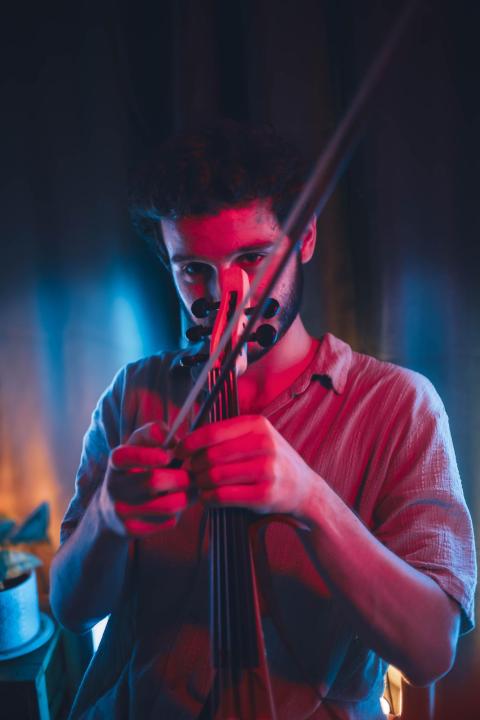 Omer Kochba playing a violin under dramatic red and blue lighting, focused intently on the instrument.